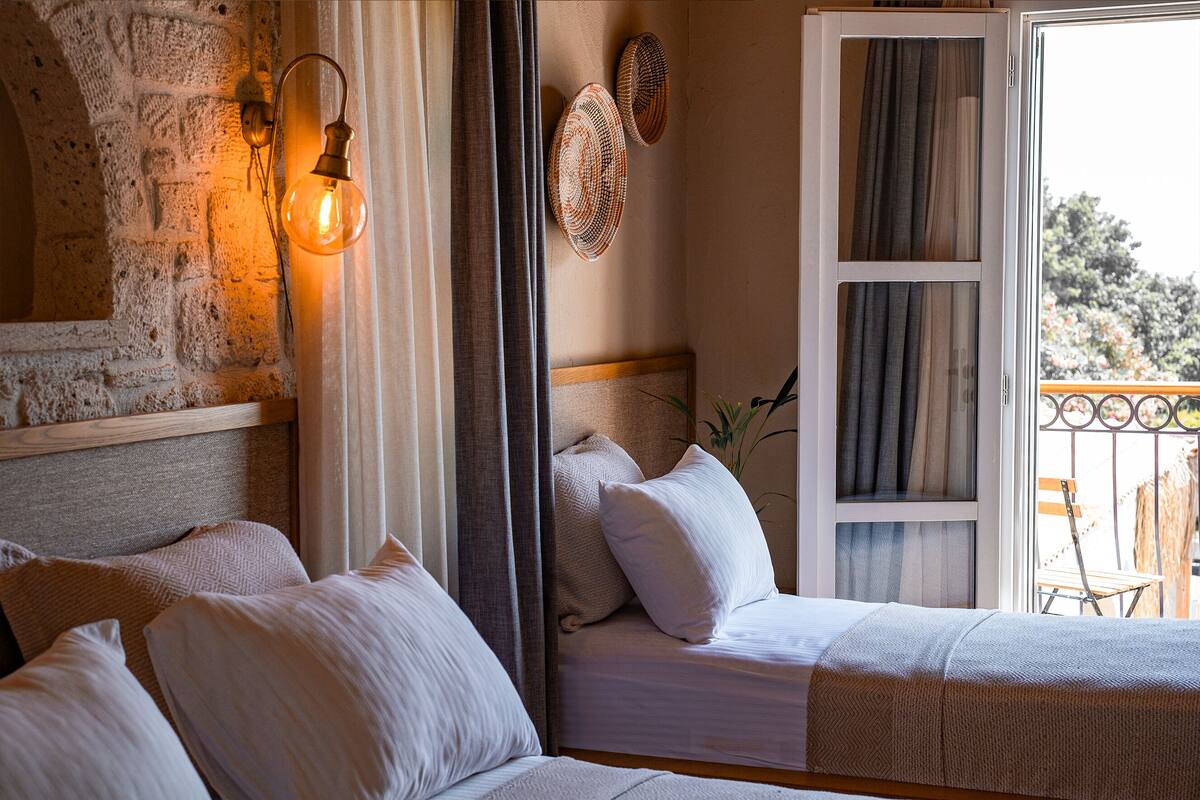 Un dormitorio con pared de piedra, cama con ropa de cama blanca, lámpara colgante y vistas al exterior.