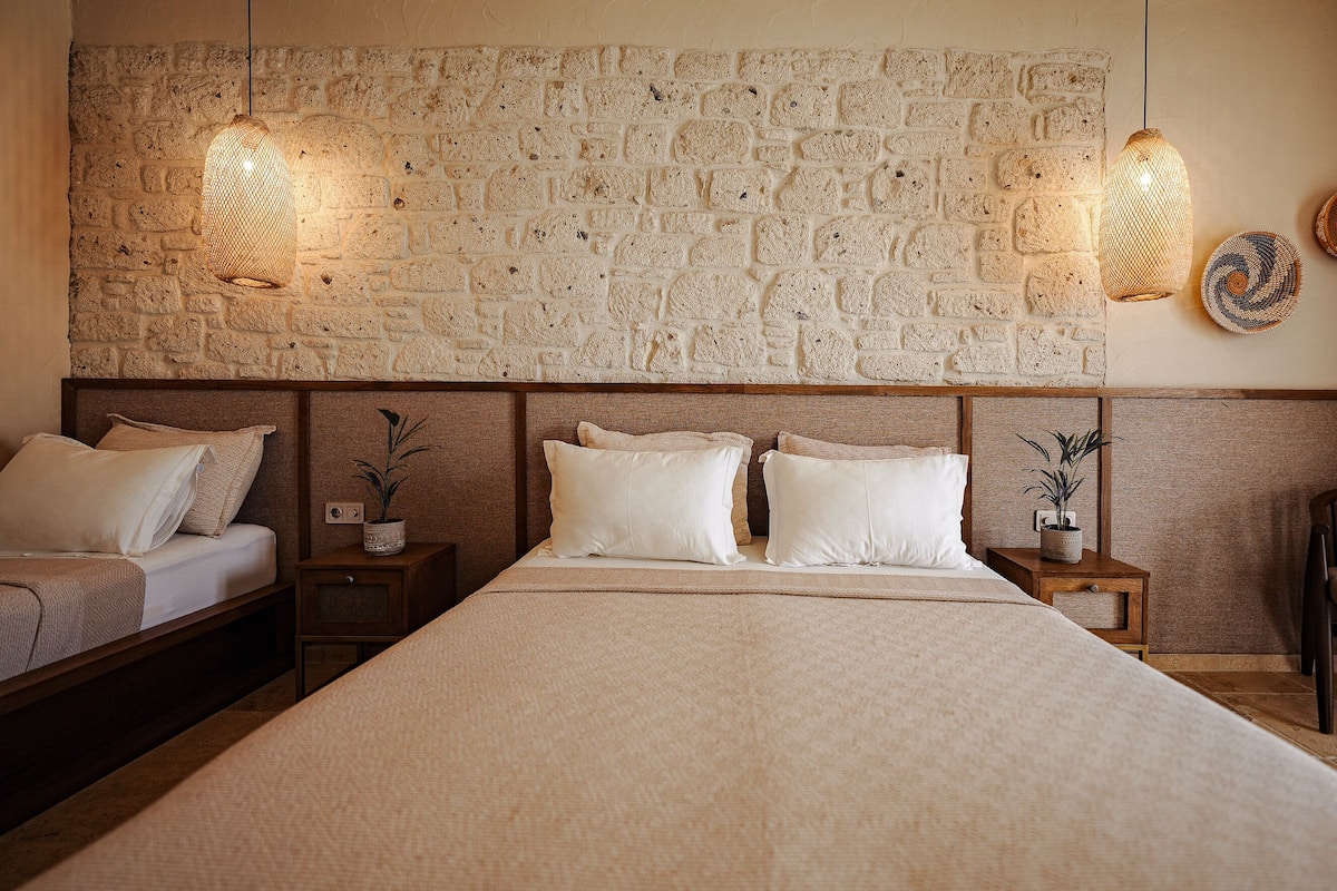 Un dormitorio con pared de piedra, dos camas, mesitas de noche y lámparas de pared.
