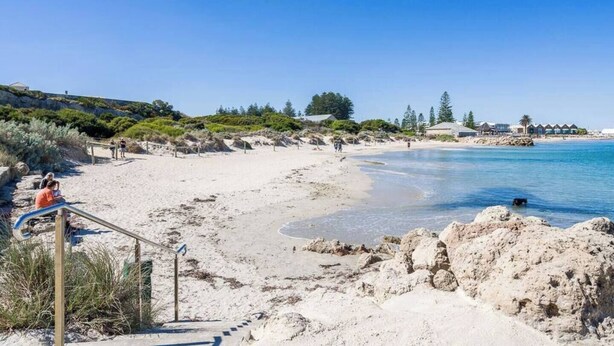 A beach with a sandy shore, clear blue water, and a few people. There are steps leading down to the beach, and some vegetation in the background. - Located in the trendy West end of Fremantle, this stylish Airbnb is perfect for beach lovers and urban explorers alike. (Fremantle)