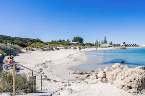 A beach with a sandy shore, clear blue water, and a few people. There are steps leading down to the beach, and some vegetation in the background. - Located in the trendy West end of Fremantle, this stylish Airbnb is perfect for beach lovers and urban explorers alike. (Fremantle)