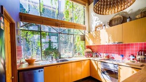 A kitchen with wooden cabinets, a red tiled backsplash, a window with a view of greenery, and a hanging light fixture. - Located in the trendy West end of Fremantle, this stylish Airbnb is perfect for beach lovers and urban explorers alike. (Fremantle)