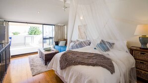 A bedroom with a canopy bed, a view to the outside, a small table, and a lamp. - Located in the trendy West end of Fremantle, this stylish Airbnb is perfect for beach lovers and urban explorers alike. (Fremantle)