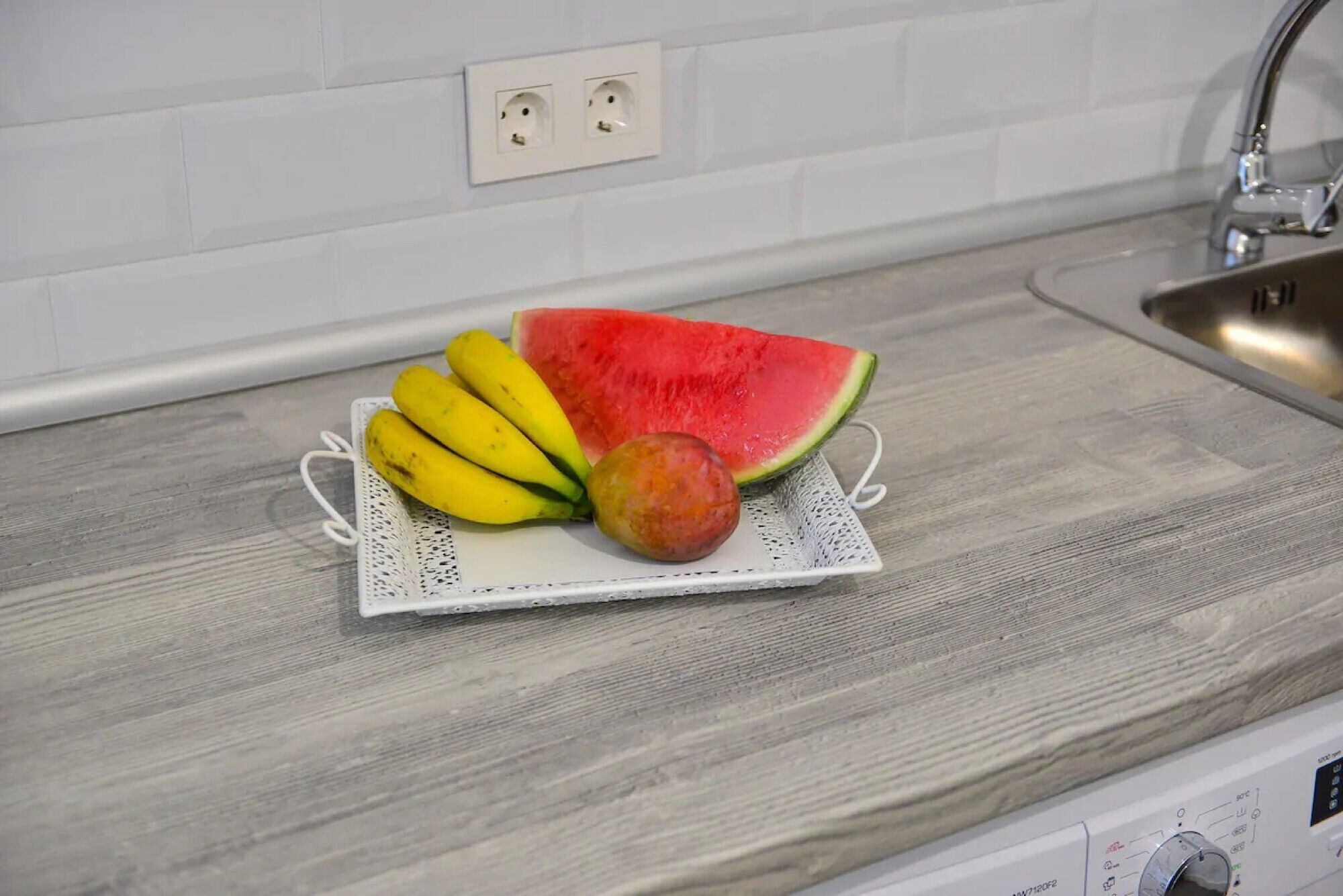 Eine Küchenarbeitsplatte mit einer Obstschale, die Bananen, ein Wassermelonenstück und einen Pfirsich enthält.