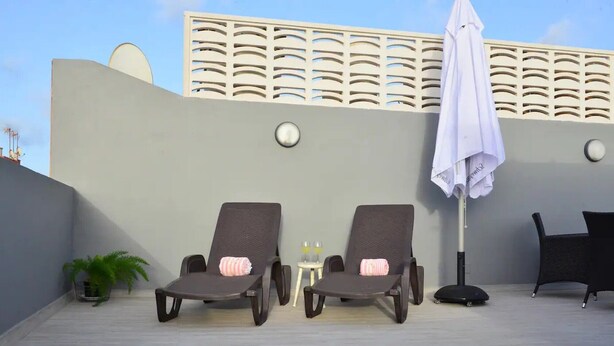 Two lounge chairs with towels, a small table with two glasses, a potted plant, and a white umbrella on a rooftop terrace. - Holiday Home Marina with Mountain View, Terrace & Wi-Fi (Las Palmas de Gran Canaria)