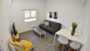 A compact living space with a sofa, a dining table with chairs, a small coffee table, a TV, and a window. - Holiday Home Marina with Mountain View, Terrace & Wi-Fi (Las Palmas de Gran Canaria)