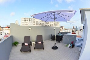 En tagterrasse med to liggestole, et bord, en stor parasol og udsigt over bybilledet.