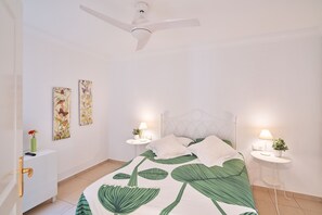 A bedroom with a bed, two bedside tables with lamps, a ceiling fan, and artwork on the wall.