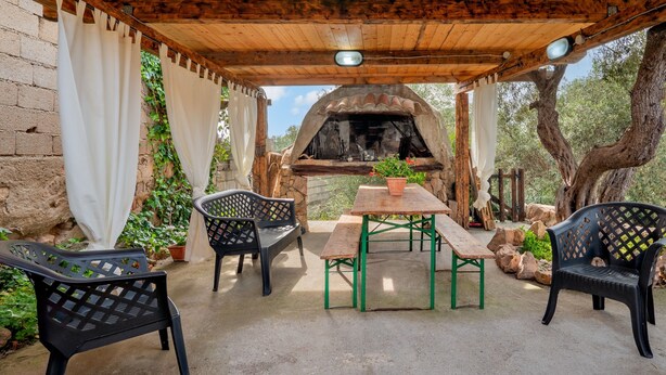 Un patio al aire libre con una pérgola de madera, un muro de piedra y un horno de ladrillo.