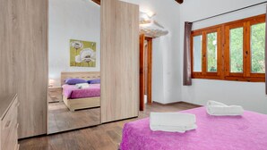 Un dormitorio con cama, armario de madera, espejo, ventana con cortinas y un cuadro en la pared.