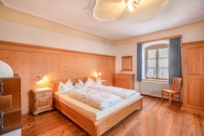 Une chambre à coucher aux murs lambrés, avec un lit, des tables de chevet, une commode et une fenêtre avec des rideaux.