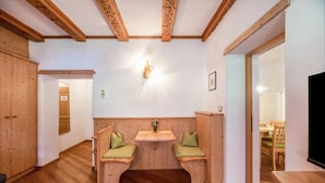 A room with wooden floors, a built-in bench with cushions, a wall-mounted light fixture, and a wooden ceiling with exposed beams.