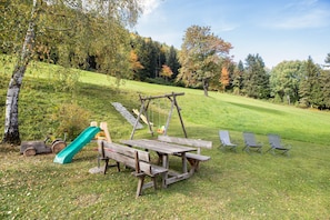 A picnic table with benches, a swing set, and a slide in a grassy park area. - 'Apartment Morgenlicht' with Balcony & Wi-Fi (Trodena)