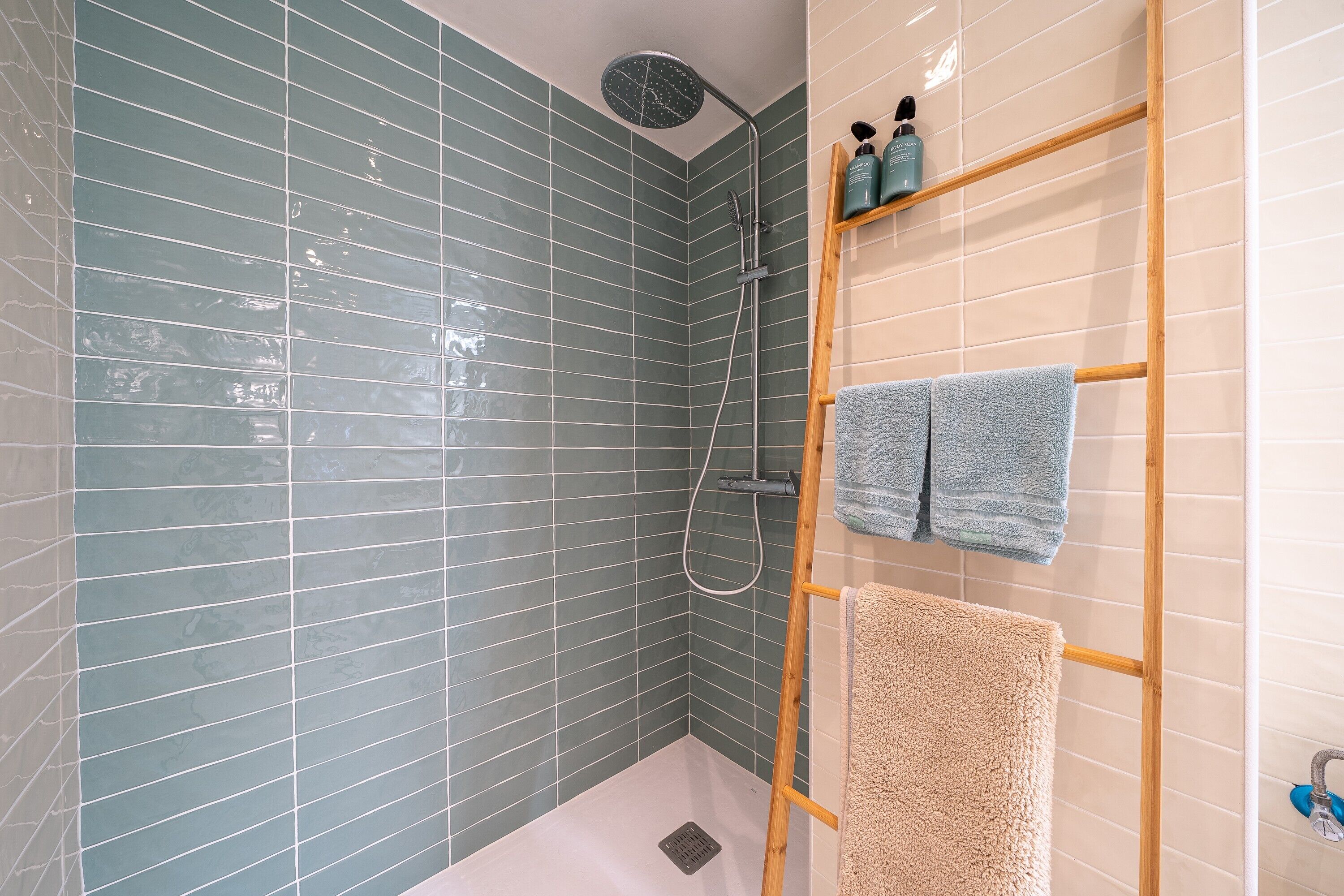 A shower with a rain showerhead, a wooden towel rack with towels, and a shelf with toiletries.