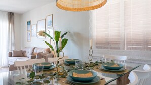 A dining area with a glass table, teal bowls, white chairs, and a wicker chandelier. - Coral Beach by Pat Apartment with Sea Views, Shared Pool, and Wi-Fi (Calafell)