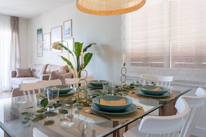 A dining area with a glass table, teal bowls, white chairs, and a wicker chandelier.