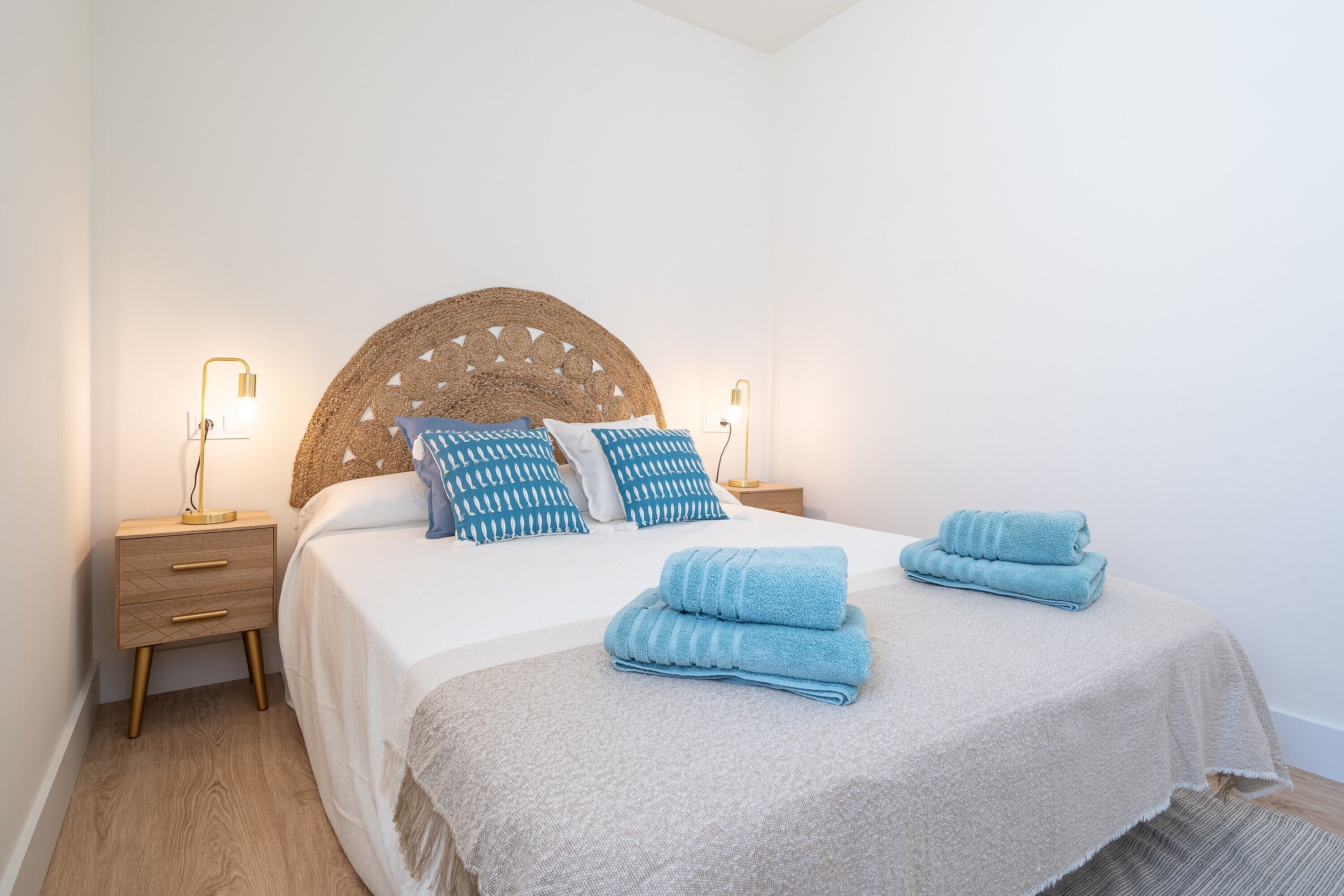 Un lit bien fait, avec une tête de lit, deux tables de chevet avec des lampes et une paire de serviettes pliées posées sur le lit.