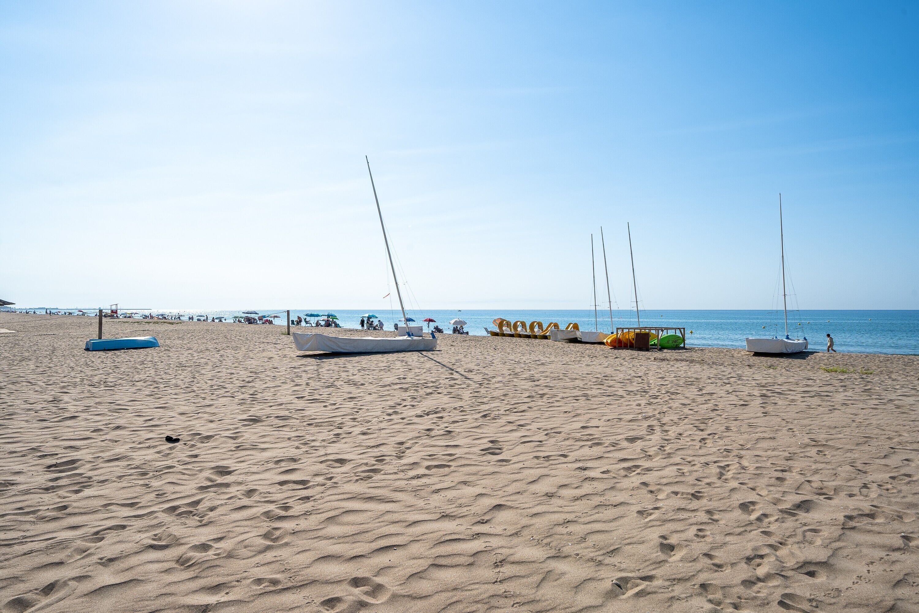 A sandy beach with several sailboats and a few people in the distance.
