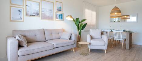 A living room with a sofa, a side table, a chair, a dining area with a table and chairs, and a hanging lamp.
