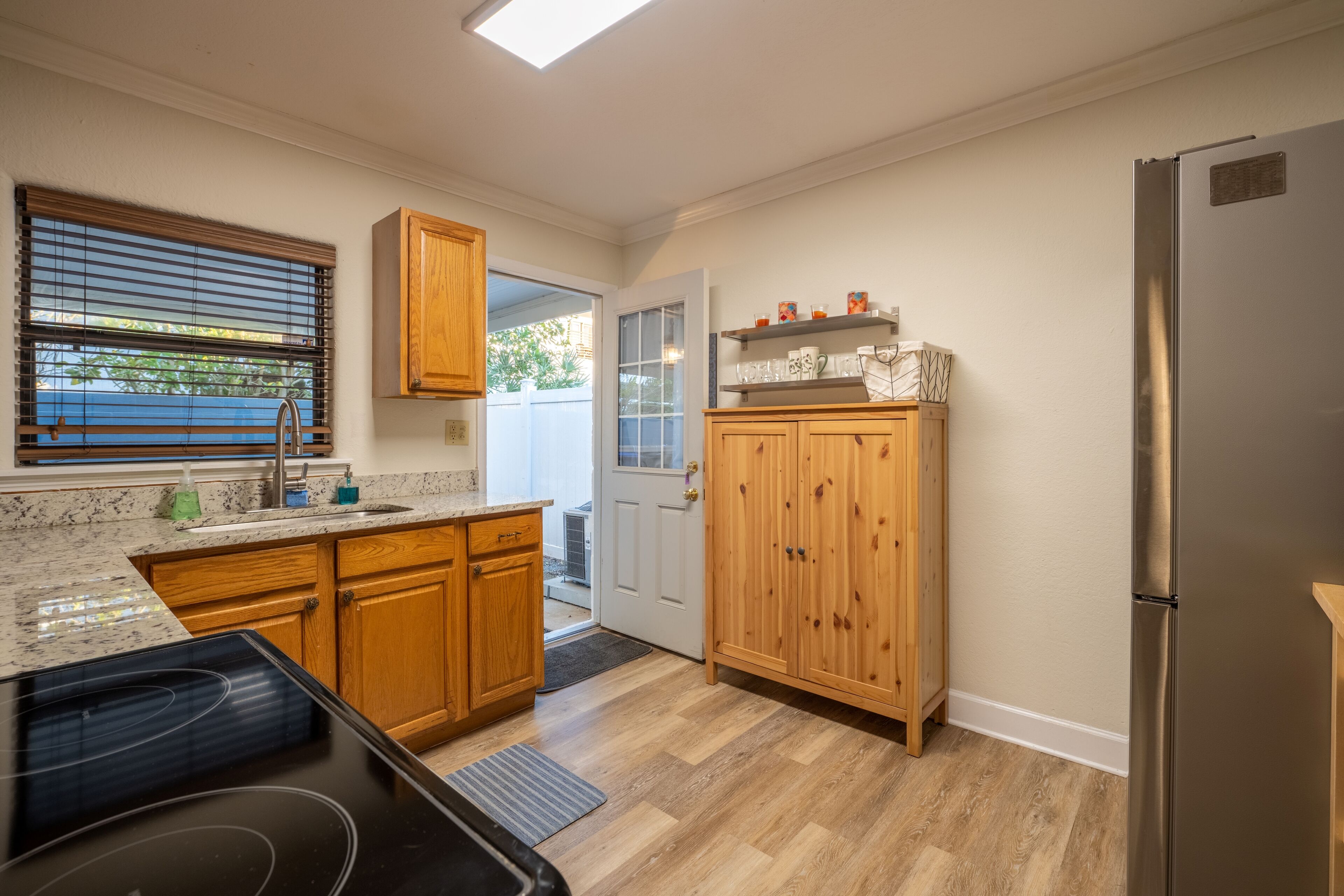 Una cocina con armarios de madera, un refrigerador de acero inoxidable y un ventanal con persianas.