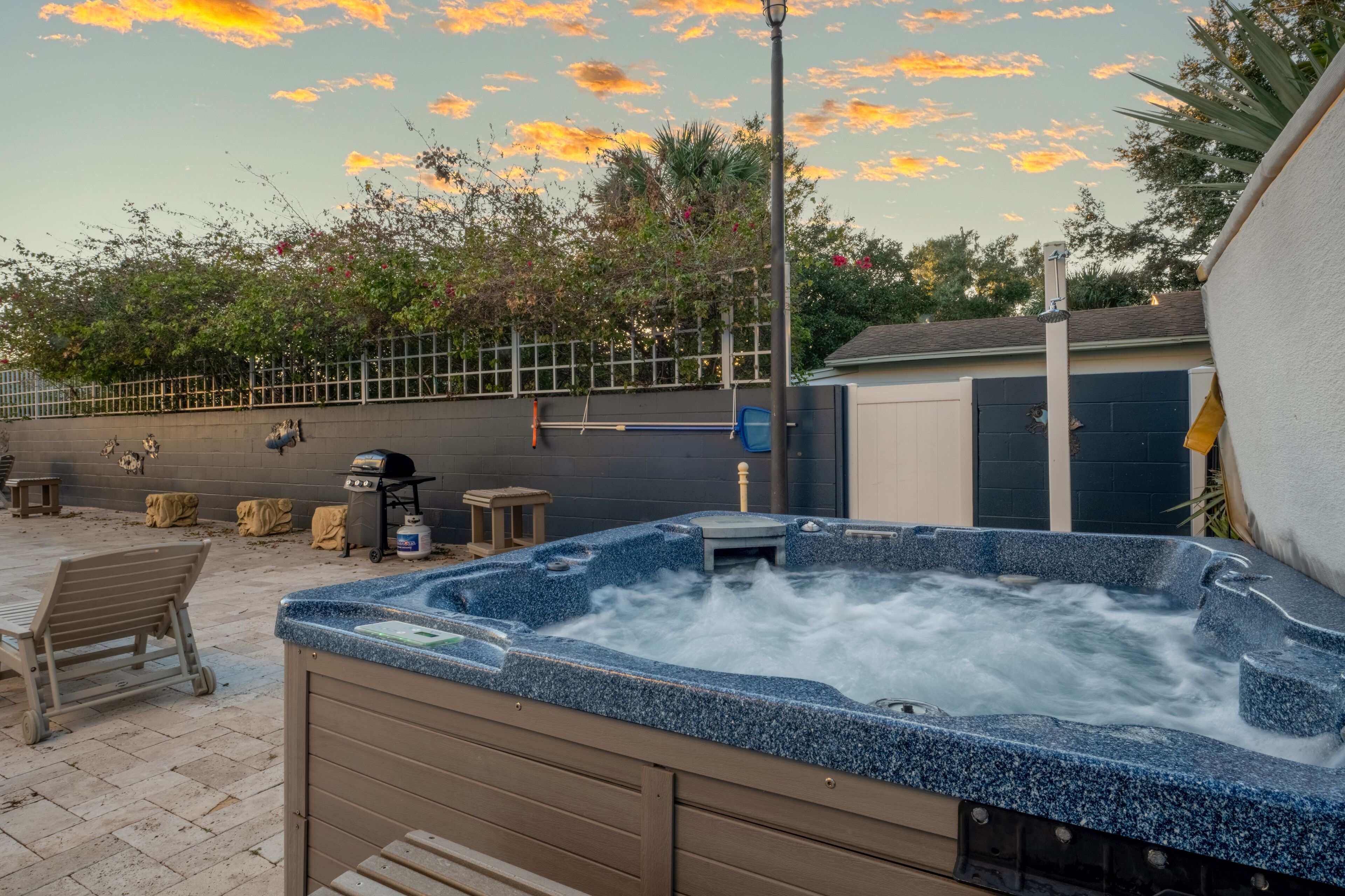 A hot tub in an outdoor setting with a patio area, a fence, and a garage in the background.