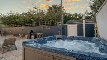 A hot tub in an outdoor setting with a patio area, a fence, and a garage in the background.