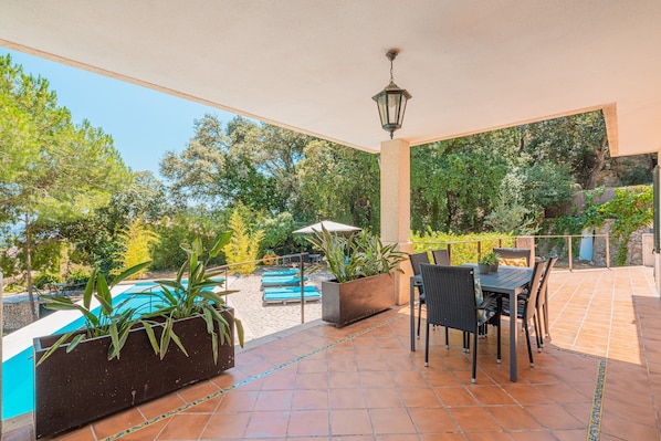Une terrasse couverte avec une piscine, des sièges d’extérieur et des plantes en pot.