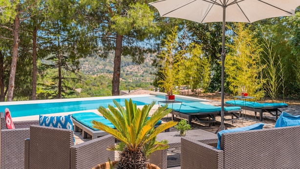 Un área junto a la piscina con sillones de descanso, una sombrilla y vistas a la piscina y árboles circundantes.
