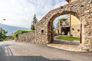 A stone archway leading to a building with a balcony, a stone wall, and a view of the mountains.