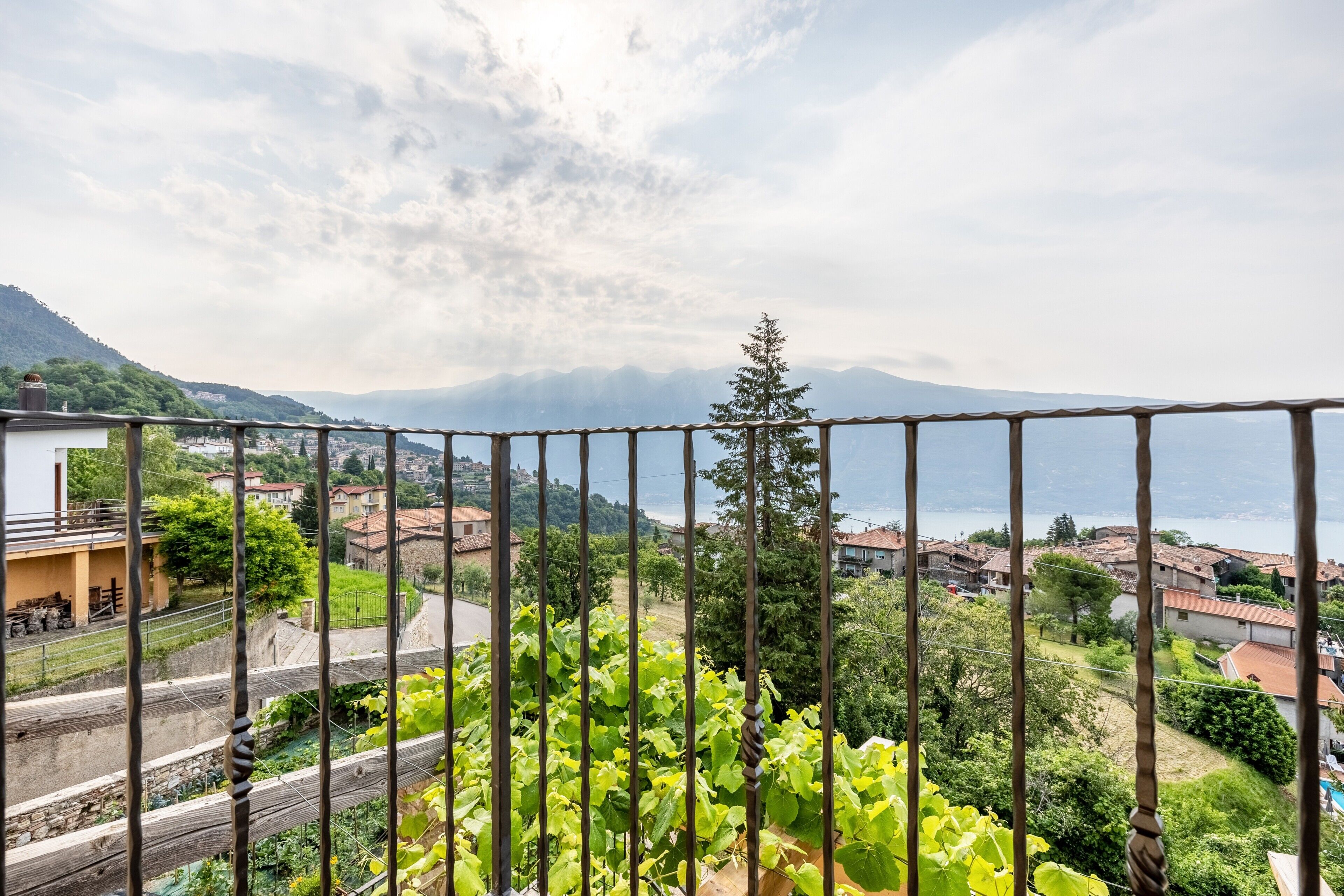 Ein Balkon mit Blick auf eine Stadt, viel Grün und Berge in der Ferne.