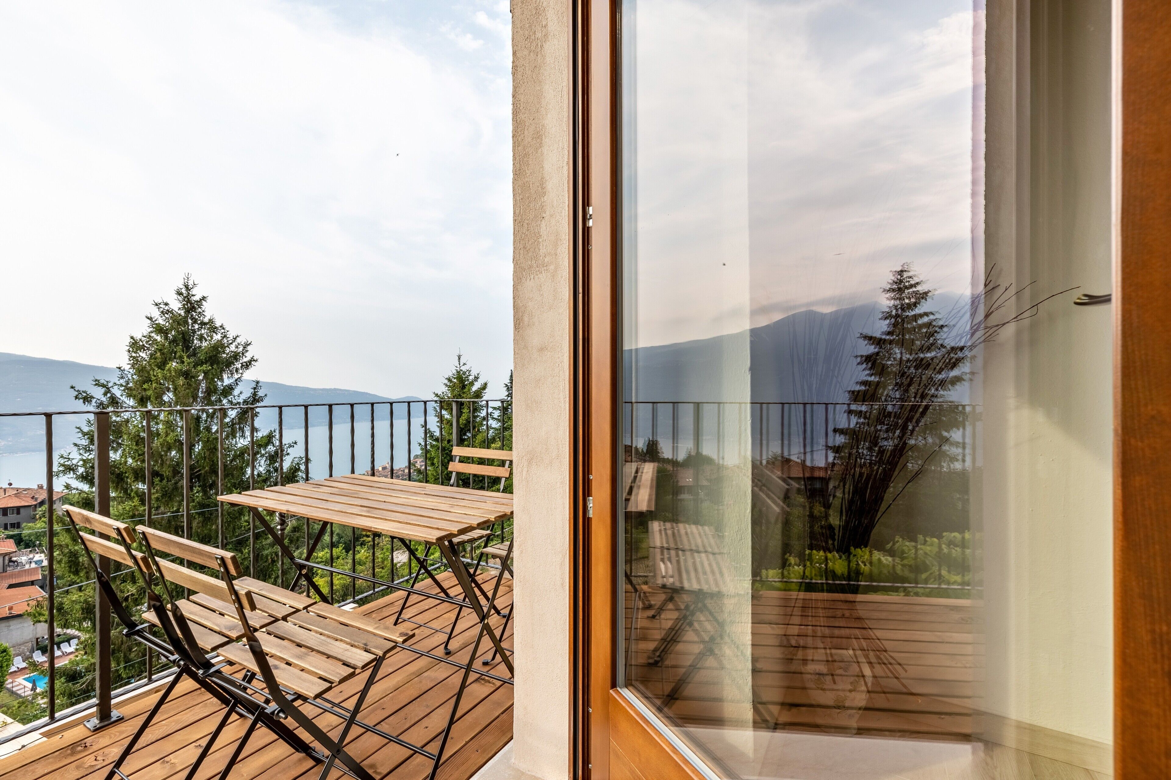 A balcony with a wooden table and chairs, a glass door, and a view of trees and buildings.