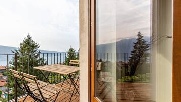 A balcony with a wooden table and chairs, a glass door, and a view of trees and buildings.