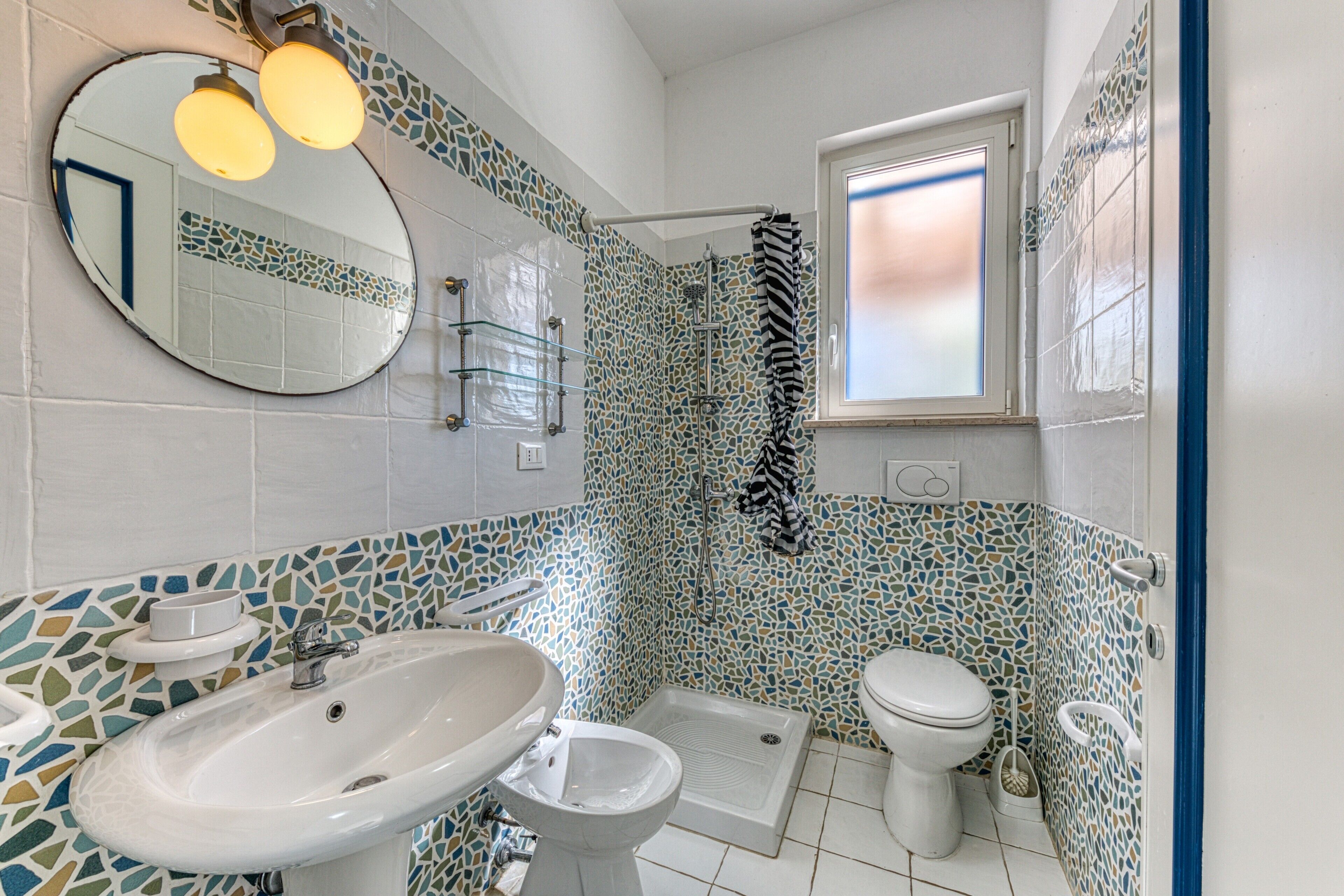 A bathroom with a sink, toilet, shower, and a mirror.