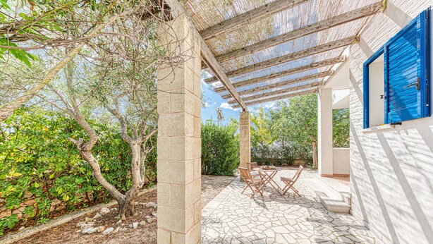 A covered patio area with stone flooring, a table with chairs, and a blue door.