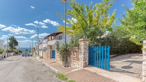 A residential street with houses, a blue gate, and a clear sky.