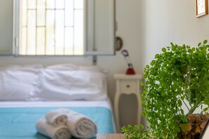 A hotel room with a bed, a window with bars, a bedside table with a lamp, and a potted plant.