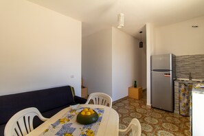 A compact living space with a dining area, a sofa, a kitchen with a refrigerator, and a patterned floor.