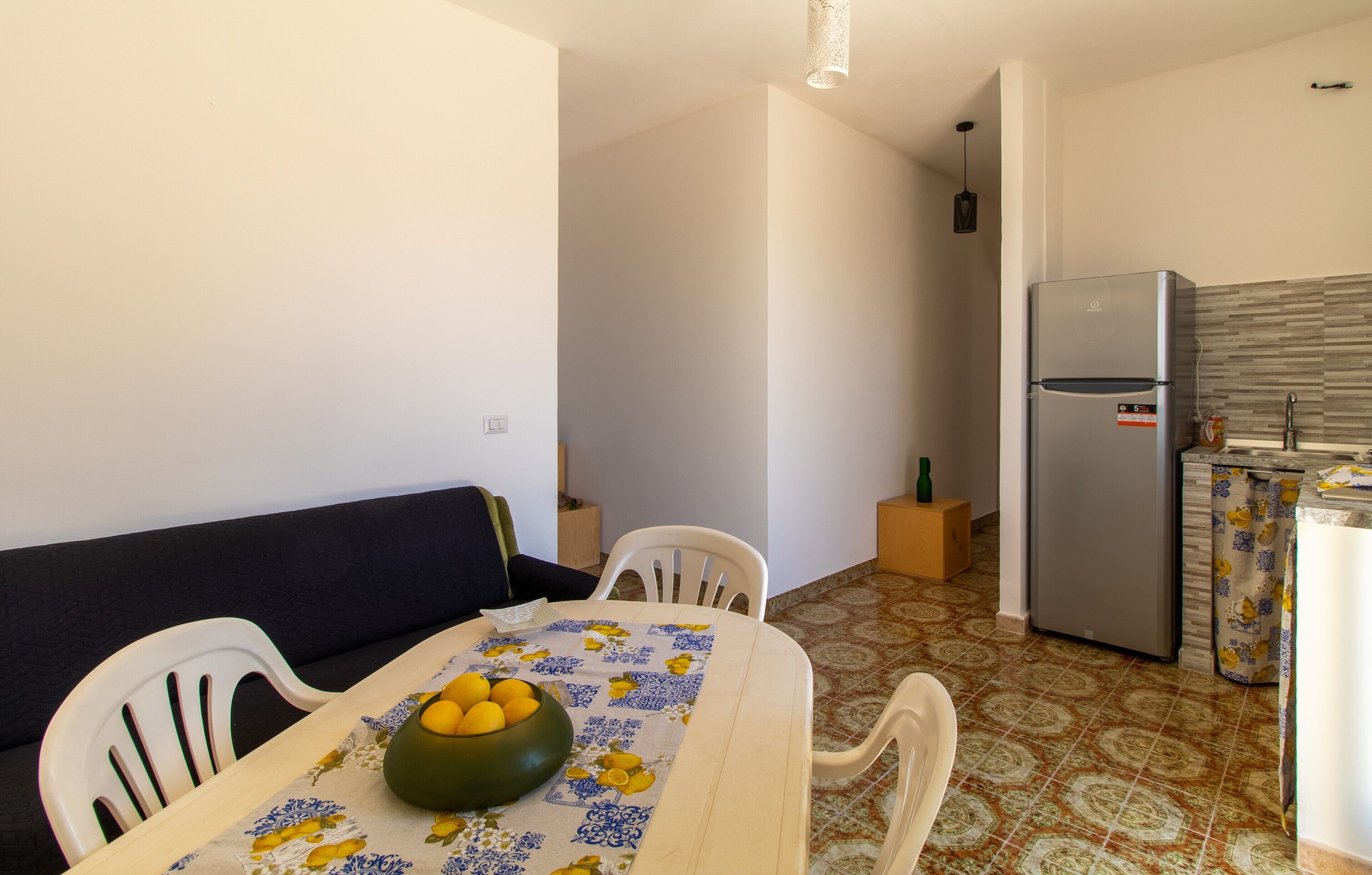 A compact kitchen with a refrigerator, a dining table with chairs, and a sofa.