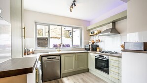 A modern kitchen with a dishwasher, oven, and a window overlooking a garden.