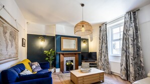 A living room with a blue sofa, a wooden coffee table, a fireplace, a television, and a large window with curtains.