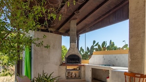 Un área de cocina al aire libre con un horno de piedra, un lavamanos y una silla de madera.