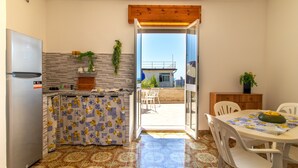 Cocina compacta con refrigerador, piso de baldosas, mesa de comedor con sillas y vista al exterior.