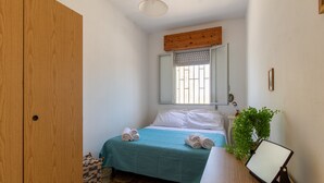 Un dormitorio con una cama, un armario de madera, una mesita con una planta y una ventana con persiana de madera.