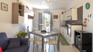 Un espacio habitable compacto con mesa de comedor, sillas, sofá, zona de cocina y ventilador de techo.