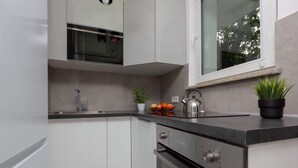 A modern kitchen with white cabinets, a stainless steel microwave, a kettle, and a potted plant. - Stylish Studio in Mokotow | Balcony | Close to Metro (Warszawa)