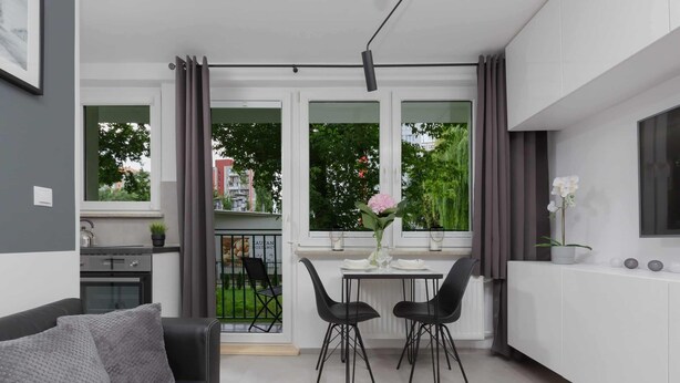 A modern kitchen with a dining area, a black sofa, and a view of the outside. - Stylish Studio in Mokotow | Balcony | Close to Metro (Warszawa)