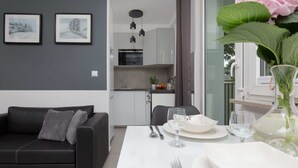 A modern living room with a black sofa, a dining table set with plates, glasses, and cutlery, and a kitchen in the background. - Stylish Studio in Mokotow | Balcony | Close to Metro (Warszawa)