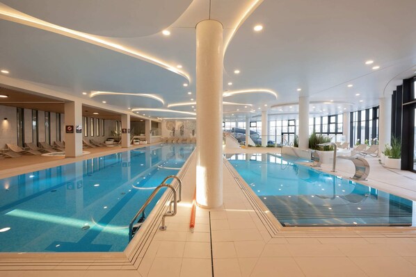 En inomhuspool med kristallklart vatten, omgiven av solstolar och med en modern takdesign.