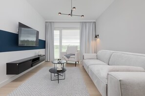 En moderne stue med et fladskærms-tv, en sofa, et sofabord og en lænestol.