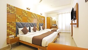 A hotel room with two beds, a wooden headboard, a ceiling fan, a TV, and a bathroom visible through a door. - MyHomeHotels – Hotel Ambrosia (New Delhi)