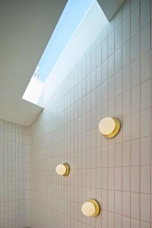 Een moderne badkamer met dakraam, betegelde wanden en drie wandlampen.